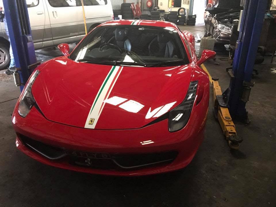 A red sports car positioned between workshop lift posts.